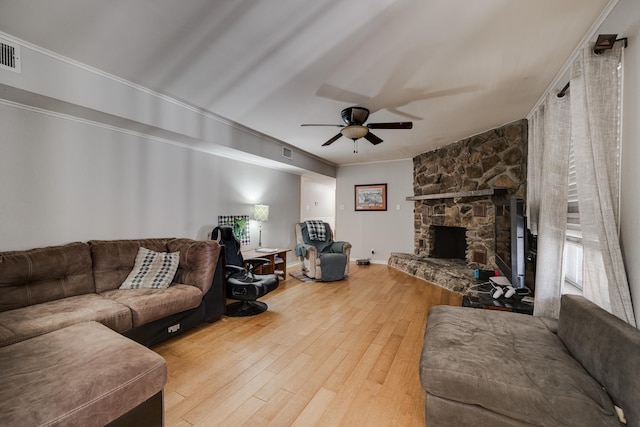 living room with crown molding, a stone fireplace, hardwood / wood-style floors, and ceiling fan