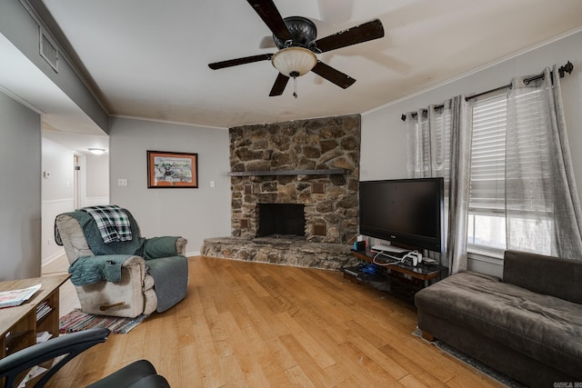 living room with hardwood / wood-style floors, a stone fireplace, ornamental molding, and ceiling fan