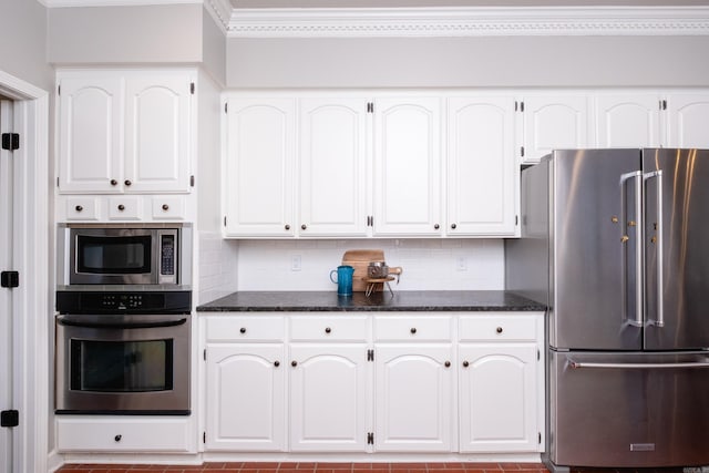 kitchen with white cabinetry, appliances with stainless steel finishes, backsplash, and dark stone countertops