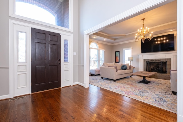 foyer entrance featuring a fireplace, hardwood / wood-style flooring, ornamental molding, a notable chandelier, and a raised ceiling