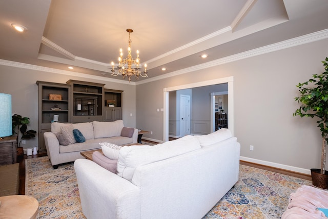 living room with a tray ceiling, wood-type flooring, ornamental molding, and a chandelier