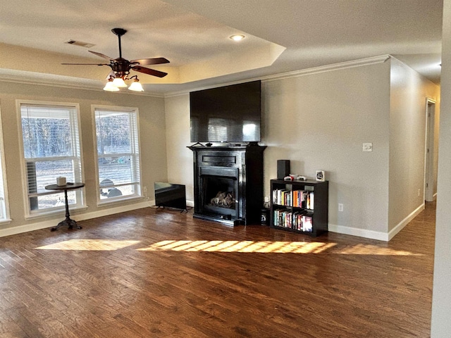 living room with a raised ceiling, ornamental molding, dark hardwood / wood-style floors, and ceiling fan