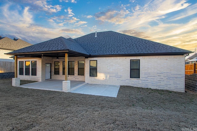 back house at dusk with ceiling fan, a yard, and a patio area