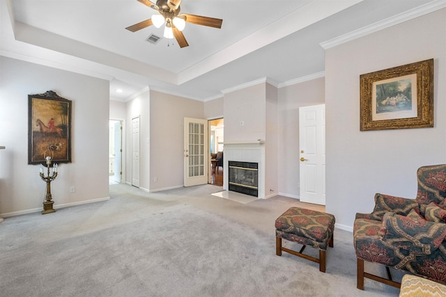 living room with a fireplace, light colored carpet, ceiling fan, a raised ceiling, and crown molding