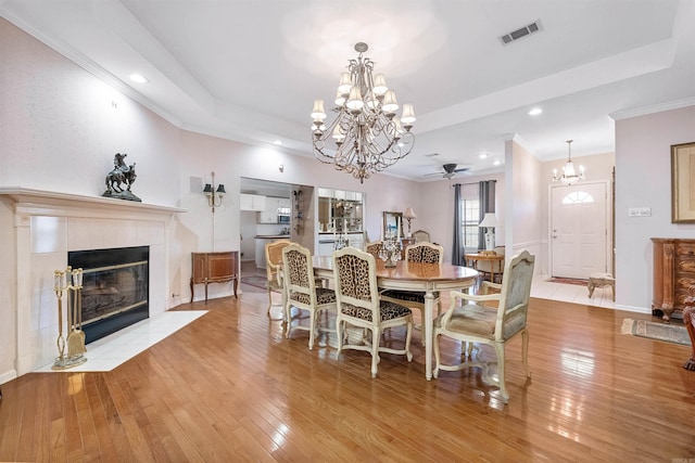 dining area with a notable chandelier, a tray ceiling, a tiled fireplace, and light wood-type flooring