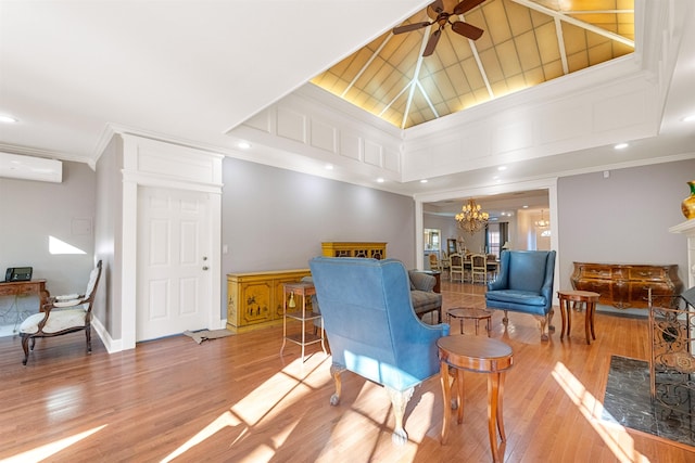 living room featuring a towering ceiling, ceiling fan with notable chandelier, a wall mounted AC, ornamental molding, and light hardwood / wood-style floors