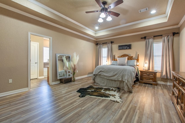 bedroom featuring ensuite bathroom, crown molding, light wood-type flooring, a raised ceiling, and ceiling fan