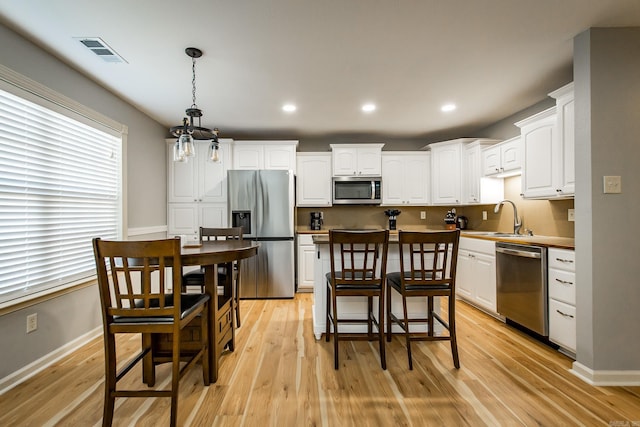 kitchen with appliances with stainless steel finishes, decorative light fixtures, sink, white cabinets, and light hardwood / wood-style flooring