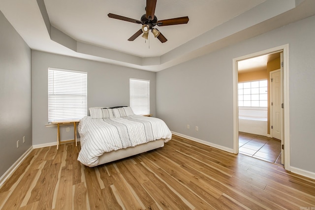 bedroom with a tray ceiling, light hardwood / wood-style floors, and ceiling fan