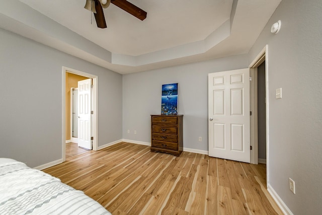 bedroom with ceiling fan, a raised ceiling, and light hardwood / wood-style floors