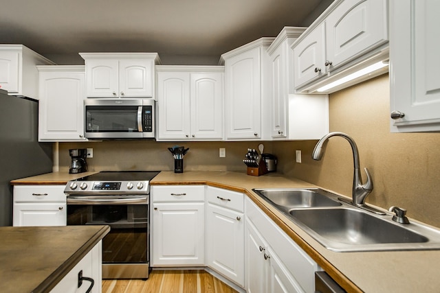 kitchen featuring appliances with stainless steel finishes, sink, light hardwood / wood-style flooring, and white cabinets