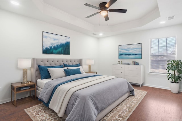 bedroom with dark hardwood / wood-style floors, ceiling fan, ornamental molding, and a tray ceiling