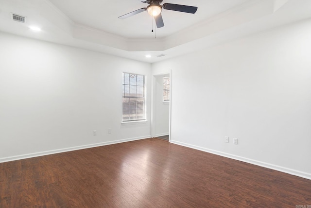 empty room featuring ornamental molding, dark hardwood / wood-style floors, ceiling fan, and a tray ceiling