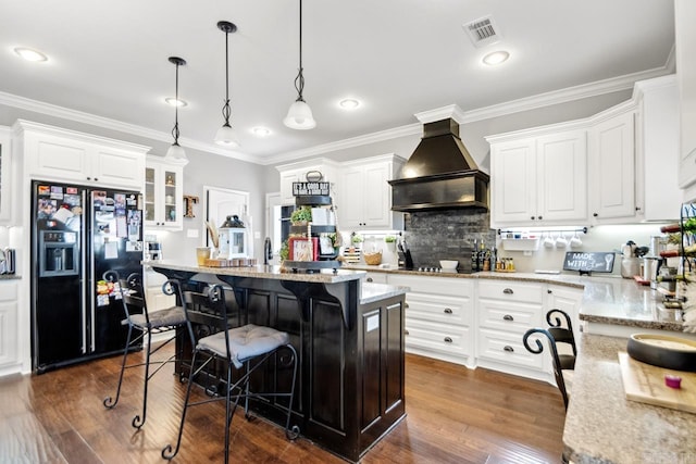 kitchen featuring white cabinetry, decorative light fixtures, black refrigerator with ice dispenser, a kitchen island, and custom range hood