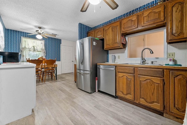 kitchen featuring sink, a textured ceiling, light wood-type flooring, appliances with stainless steel finishes, and ceiling fan