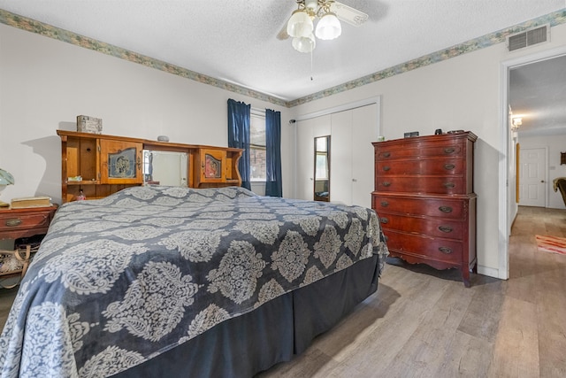 bedroom featuring light hardwood / wood-style floors, a textured ceiling, ceiling fan, and a closet