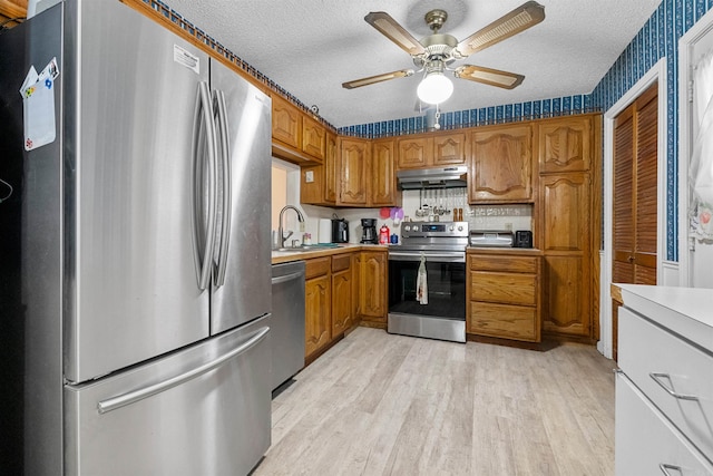 kitchen with appliances with stainless steel finishes, sink, a textured ceiling, and light hardwood / wood-style flooring