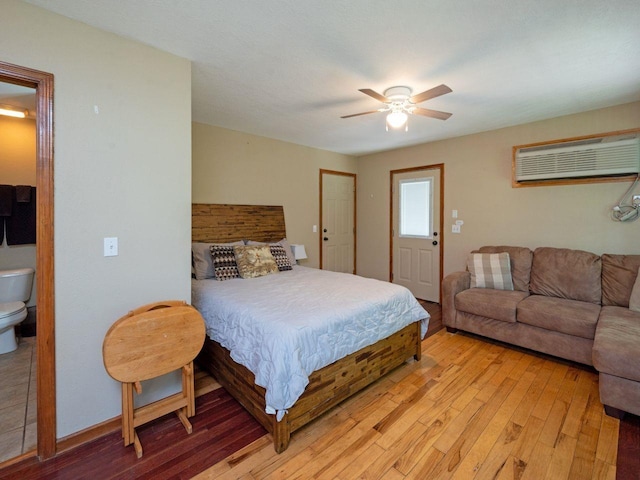 bedroom with hardwood / wood-style flooring, a wall unit AC, ceiling fan, and ensuite bath