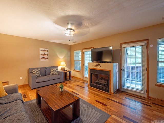 living room featuring hardwood / wood-style flooring, ceiling fan, and a textured ceiling