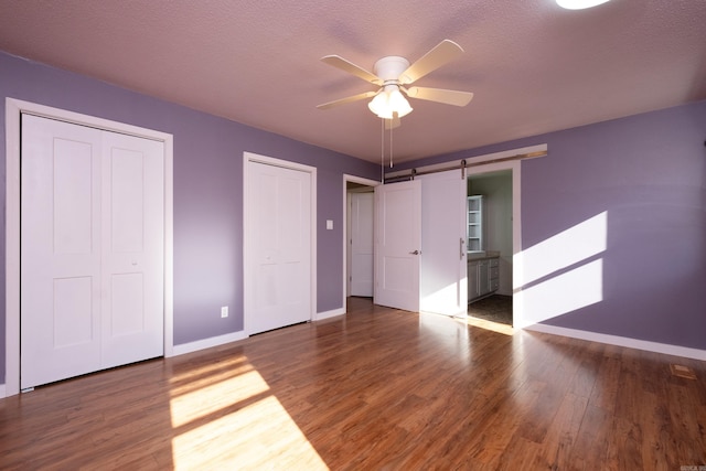 unfurnished bedroom with hardwood / wood-style floors, ceiling fan, multiple closets, a barn door, and a textured ceiling