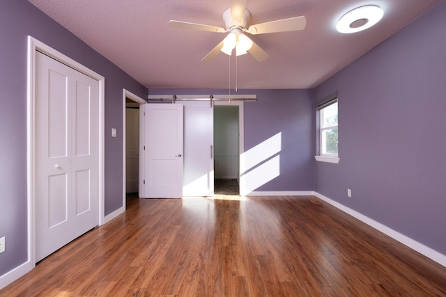 unfurnished bedroom with dark wood-type flooring, ceiling fan, a barn door, and a closet