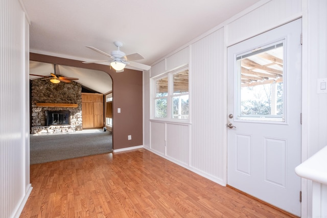 interior space with ceiling fan, a stone fireplace, vaulted ceiling, and light hardwood / wood-style flooring