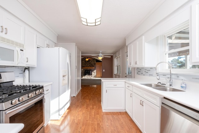 kitchen with sink, a brick fireplace, appliances with stainless steel finishes, kitchen peninsula, and white cabinets