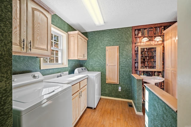 laundry area featuring sink, cabinets, washer and clothes dryer, a textured ceiling, and light hardwood / wood-style flooring