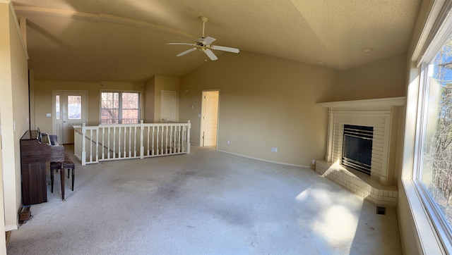 unfurnished living room with lofted ceiling, ceiling fan, a brick fireplace, light carpet, and a textured ceiling