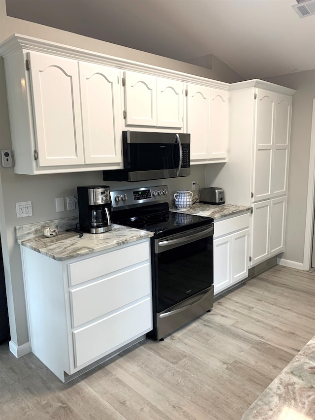 kitchen with lofted ceiling, appliances with stainless steel finishes, white cabinetry, light stone counters, and light wood-type flooring