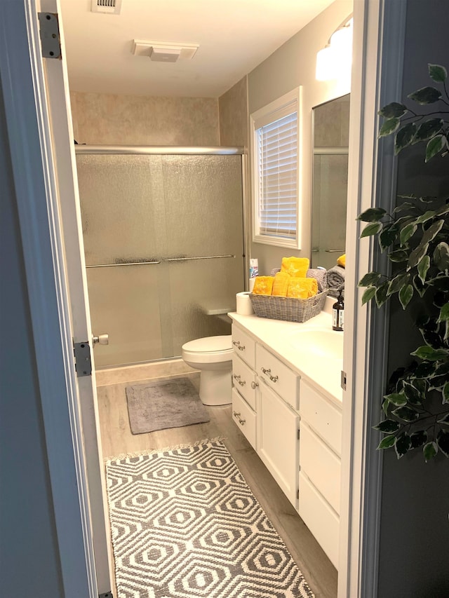 bathroom featuring vanity, wood-type flooring, a shower with door, and toilet