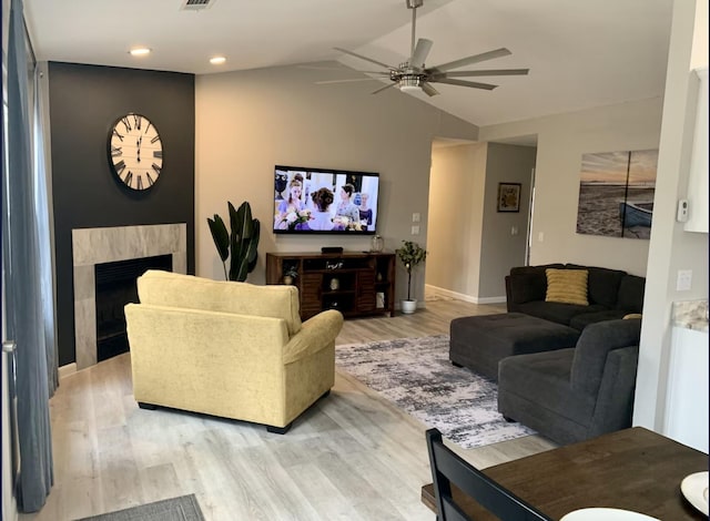 living room with ceiling fan, lofted ceiling, a fireplace, and light wood-type flooring