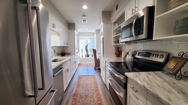 kitchen featuring sink, light stone counters, white cabinets, stainless steel appliances, and backsplash