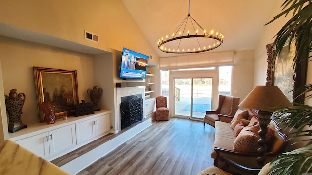 living room featuring built in features, vaulted ceiling, a notable chandelier, and light hardwood / wood-style flooring