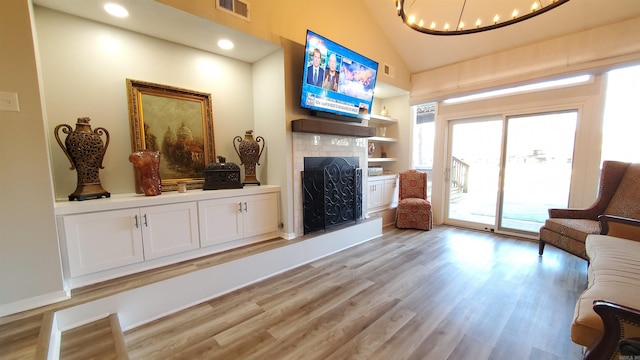 sitting room featuring lofted ceiling, an inviting chandelier, a fireplace, built in shelves, and light wood-type flooring