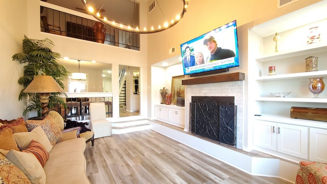 living room with a towering ceiling, a fireplace, light wood-type flooring, and built in shelves