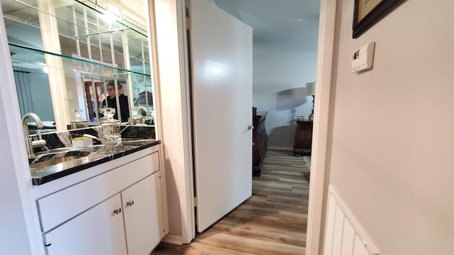 bar with sink, light hardwood / wood-style floors, and white cabinets