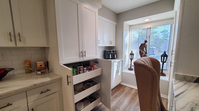 kitchen featuring white cabinetry, decorative backsplash, light stone counters, and light hardwood / wood-style flooring