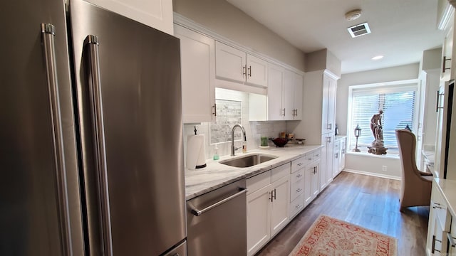 kitchen with sink, appliances with stainless steel finishes, white cabinetry, light stone countertops, and decorative backsplash