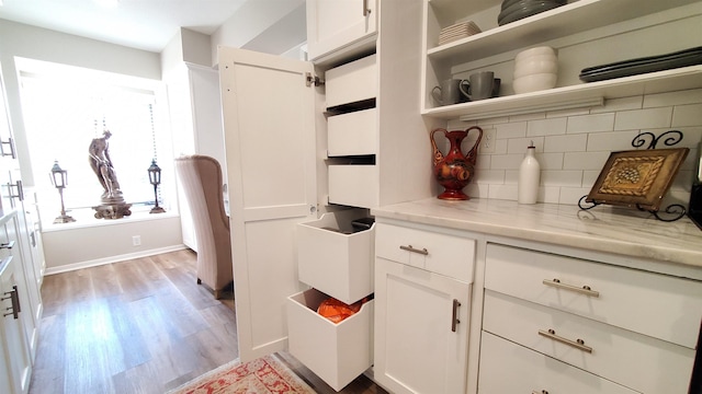 kitchen featuring light wood-type flooring, backsplash, white cabinets, and light stone counters