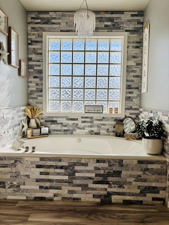 bathroom featuring a notable chandelier, wood-type flooring, and tiled tub