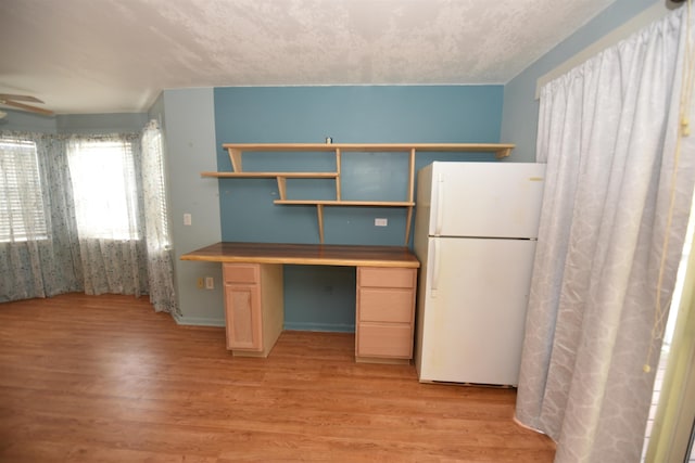 kitchen featuring light hardwood / wood-style flooring, ceiling fan, white refrigerator, built in desk, and light brown cabinets