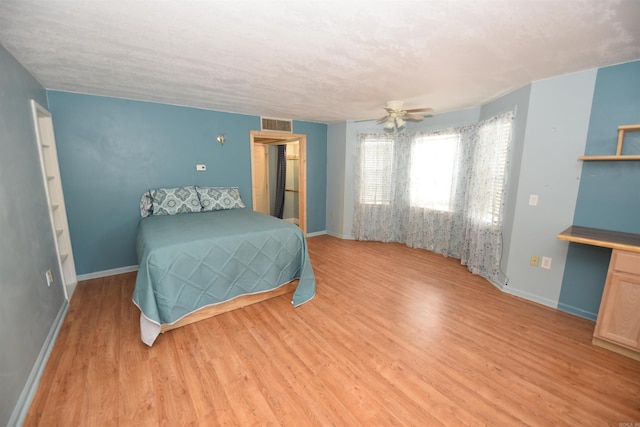 bedroom with built in desk, a textured ceiling, ceiling fan, and light hardwood / wood-style floors