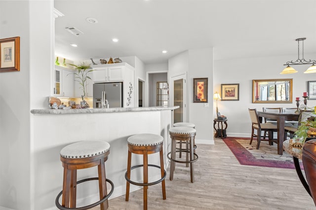 kitchen with pendant lighting, stainless steel fridge, white cabinets, kitchen peninsula, and light wood-type flooring