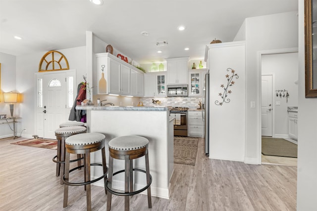 kitchen featuring appliances with stainless steel finishes, tasteful backsplash, white cabinetry, kitchen peninsula, and light hardwood / wood-style flooring