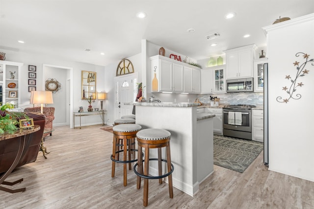 kitchen with stainless steel appliances, light hardwood / wood-style floors, white cabinets, decorative backsplash, and kitchen peninsula