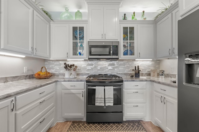 kitchen featuring light stone counters, tasteful backsplash, appliances with stainless steel finishes, light hardwood / wood-style floors, and white cabinets