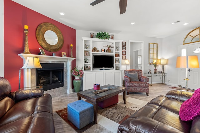 living room with ceiling fan, a tiled fireplace, and light wood-type flooring