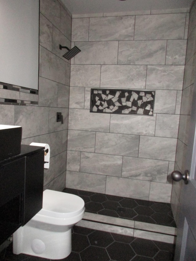 bathroom with tiled shower, vanity, toilet, and tile patterned flooring