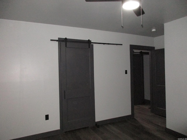 unfurnished bedroom with ceiling fan, a barn door, and dark hardwood / wood-style flooring